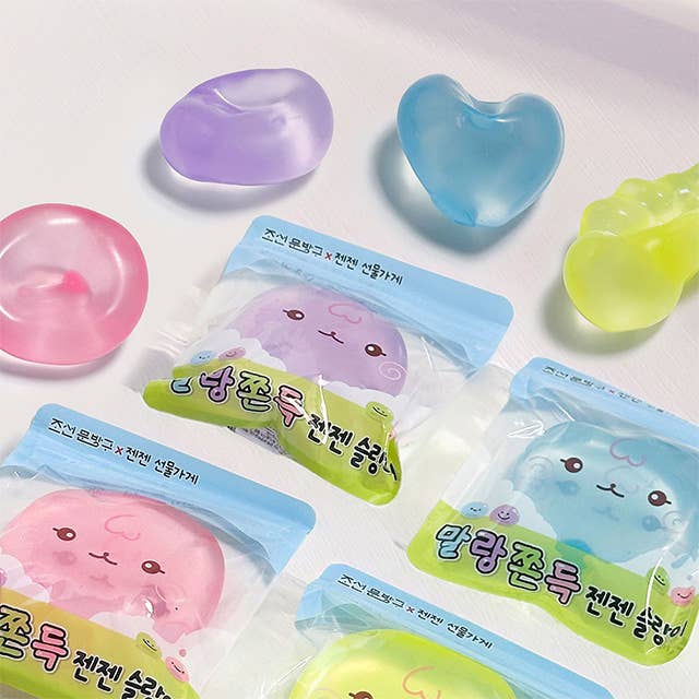 Several translucent, squishy gel-like accessories in pastel colors are arranged on a white surface, with some still in clear plastic packaging. The pieces include pink, purple, blue, and yellow shapes, and the packages have Korean text and cartoon faces.