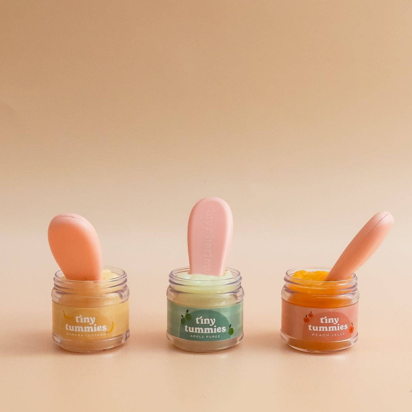 Three small jars with colorful contents and spoons on a beige background