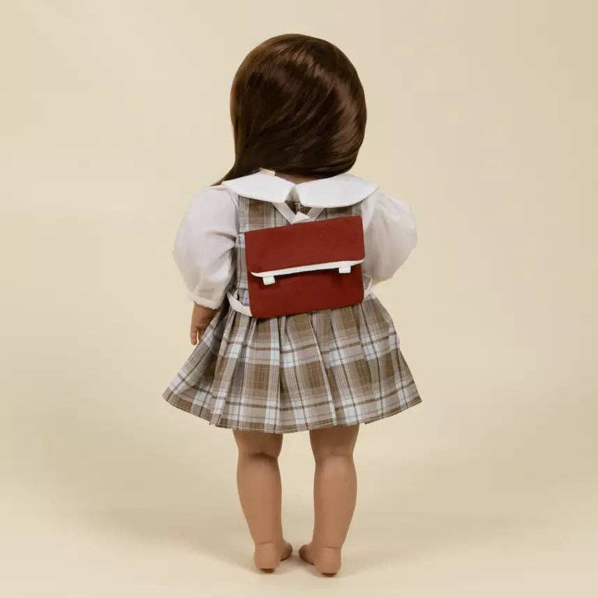 Child wearing a plaid skirt and white shirt with a red bag on a beige background