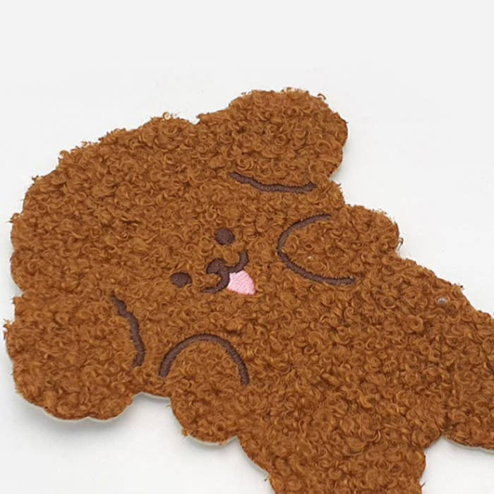 A brown textured plush or sherpa dog-shaped mat with embroidered facial features, shown on a plain white background.
