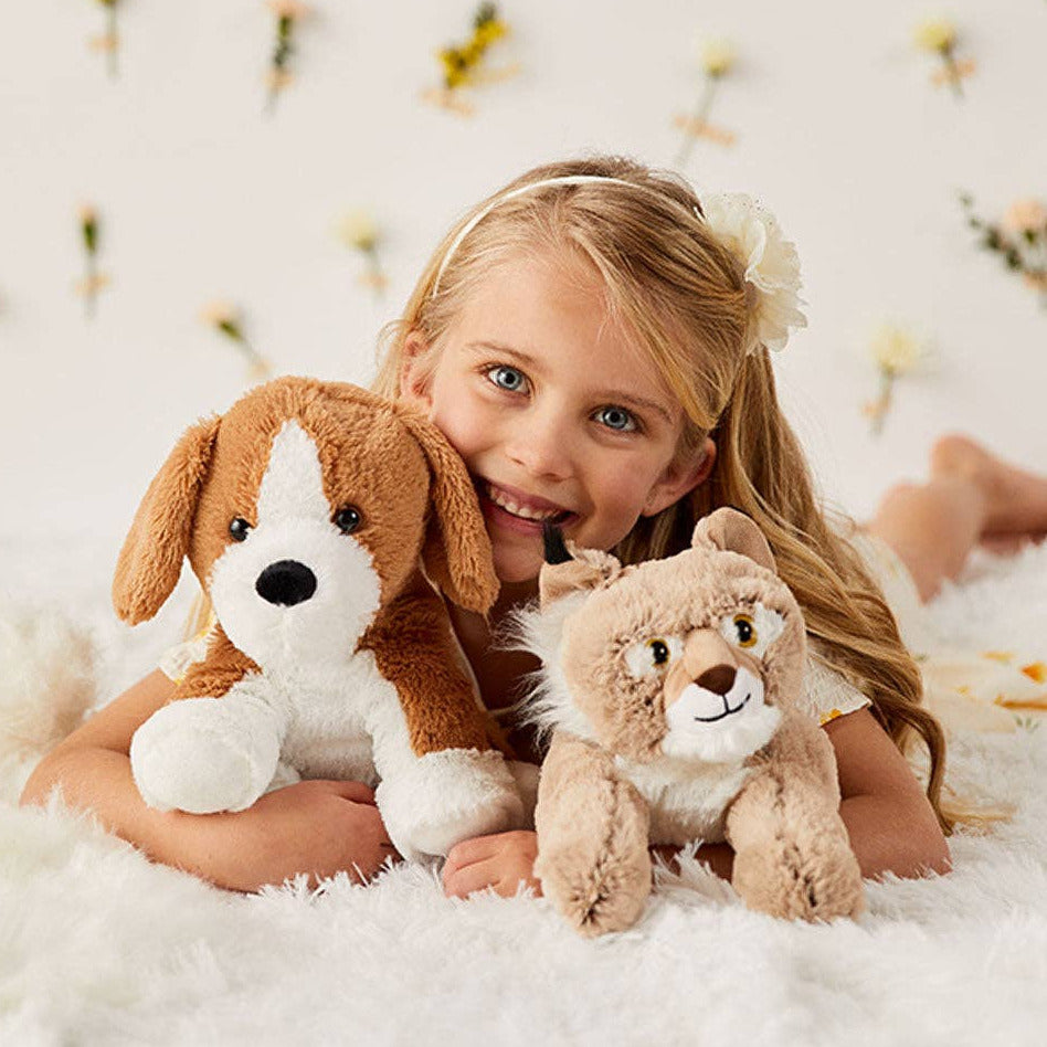 Young girl holding two plush toys on a soft surface with a floral background