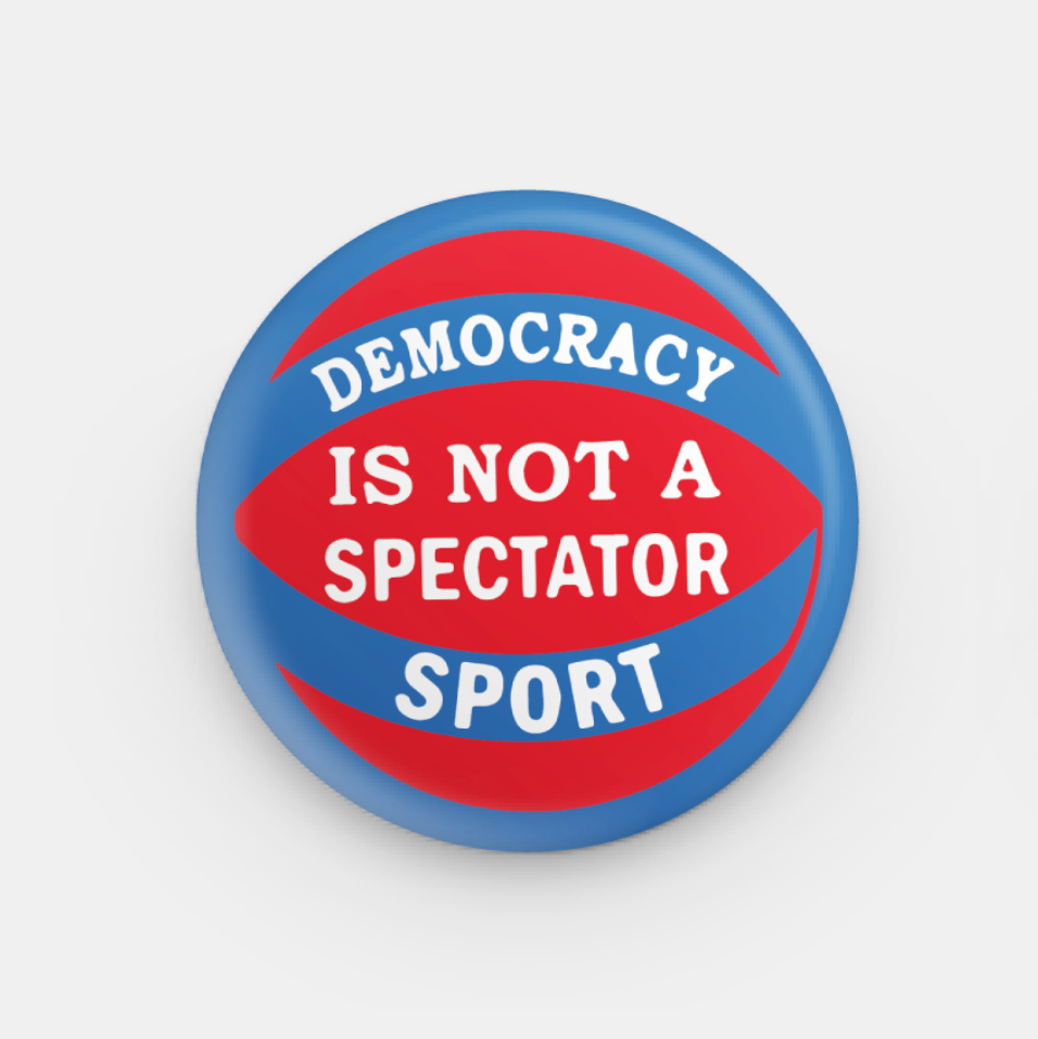Button badge with 'Democracy is not a spectator sport' text on a white background