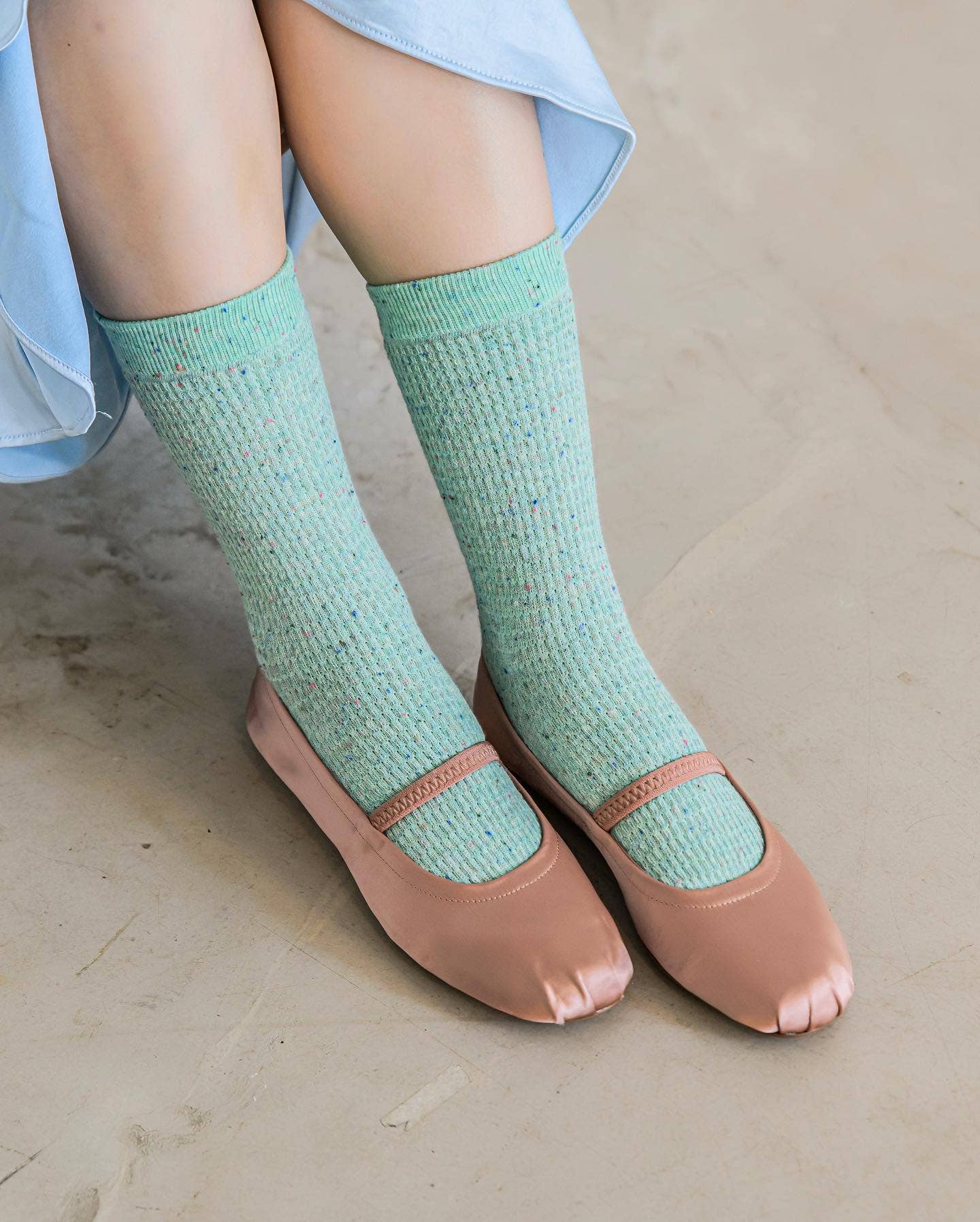 Person wearing light green socks and pink open-toe shoes on a neutral background