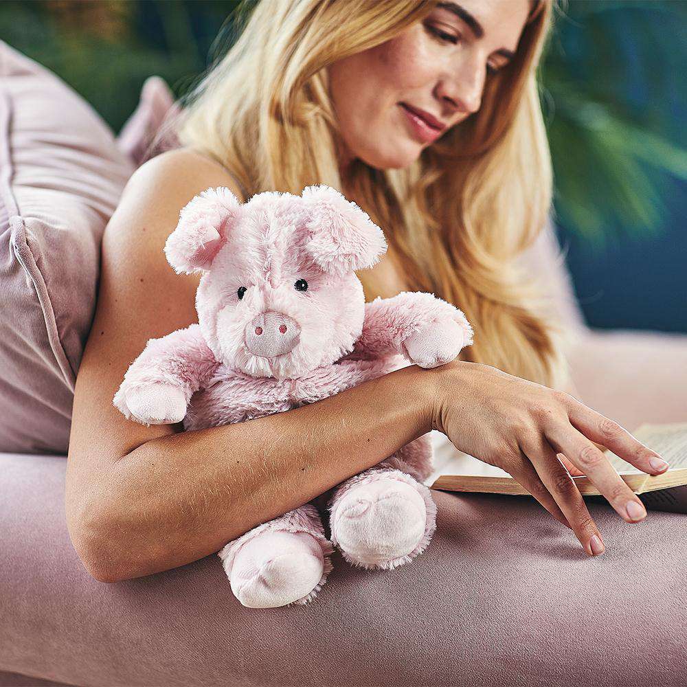 Woman reading a book with a pink plush pig toy on a couch