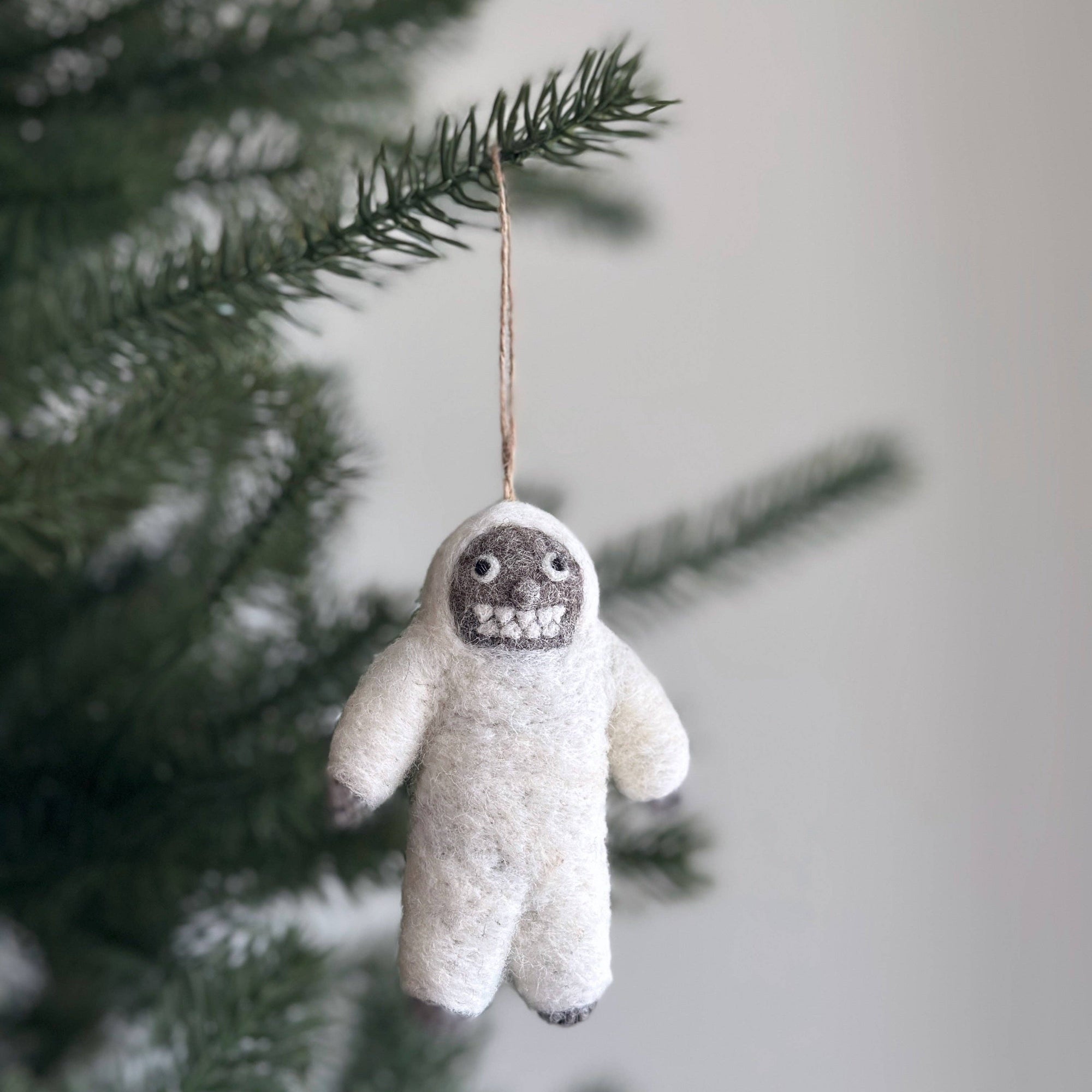 Felted creature ornament hanging on a Christmas tree branch