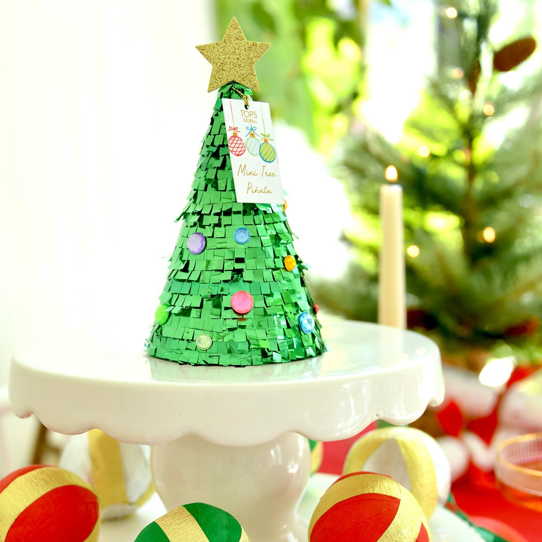Decorative Christmas tree and ornaments on a white surface with a blurred festive background.
