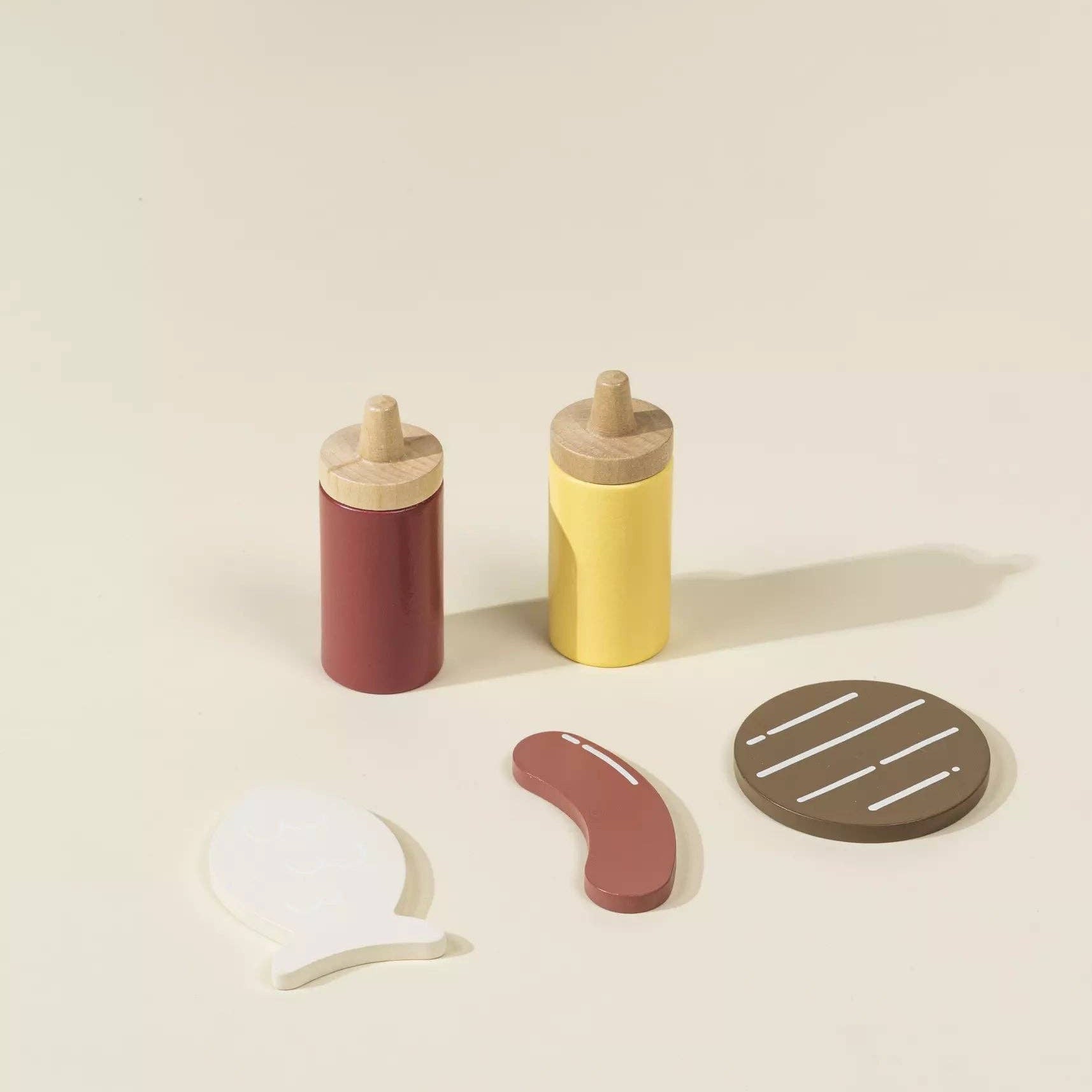 Set of toy condiment bottles with a hot dog and bun on a beige background