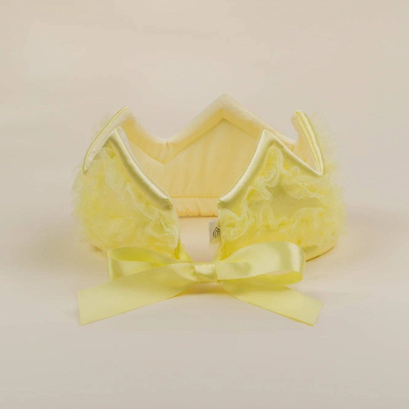 A pale yellow ruffled headband with a matching satin bow, displayed on a neutral cream background.