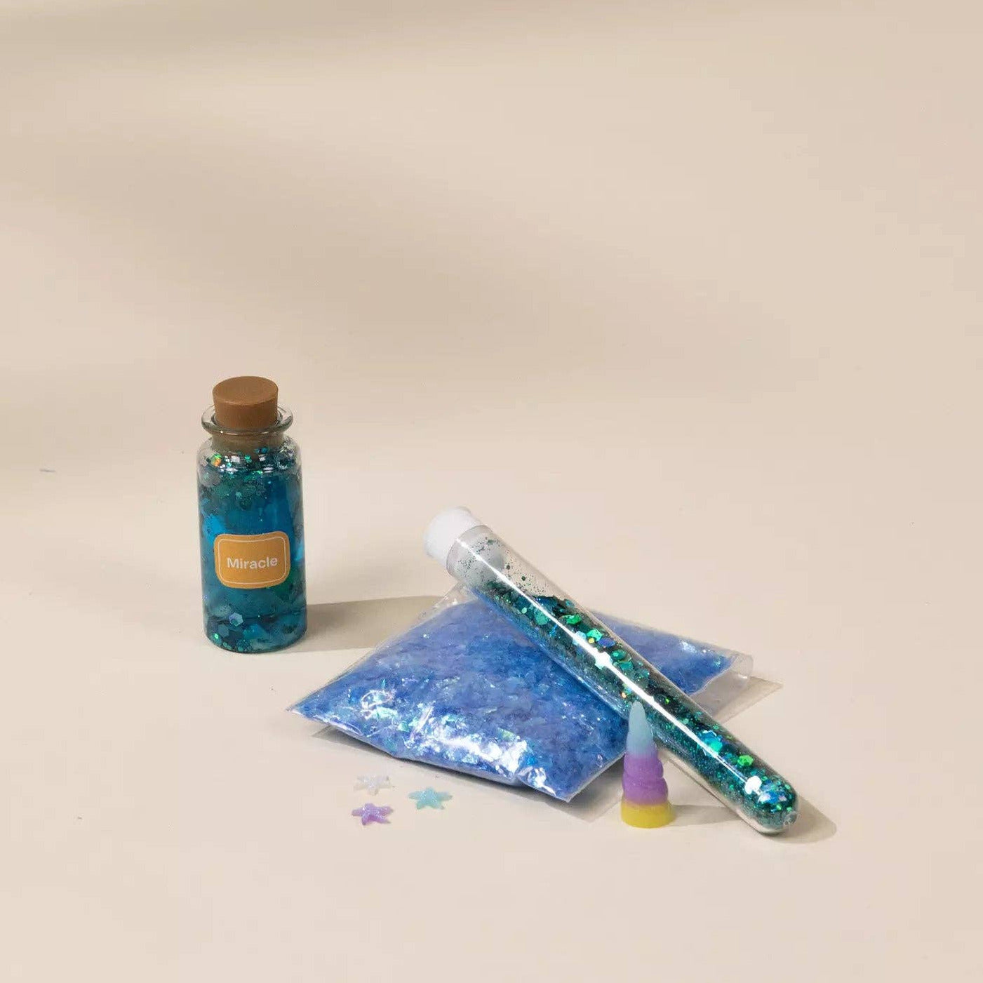 Blue glittery bottle, bag, and tube on a beige background