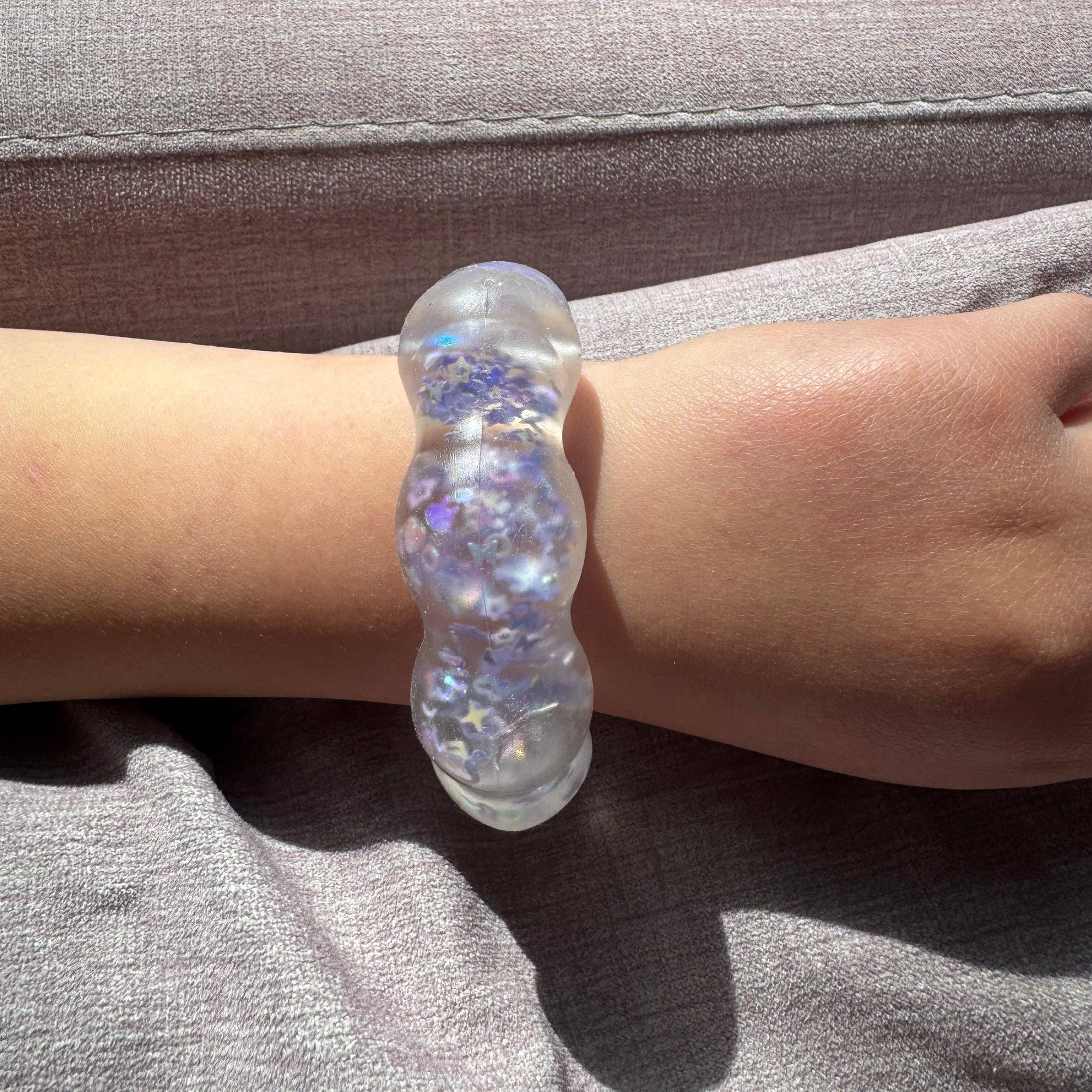 Clear bracelet with embedded stones on a wrist against a gray background