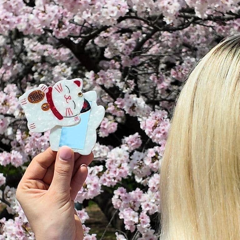 Person holding a lucky cat charm in front of cherry blossoms