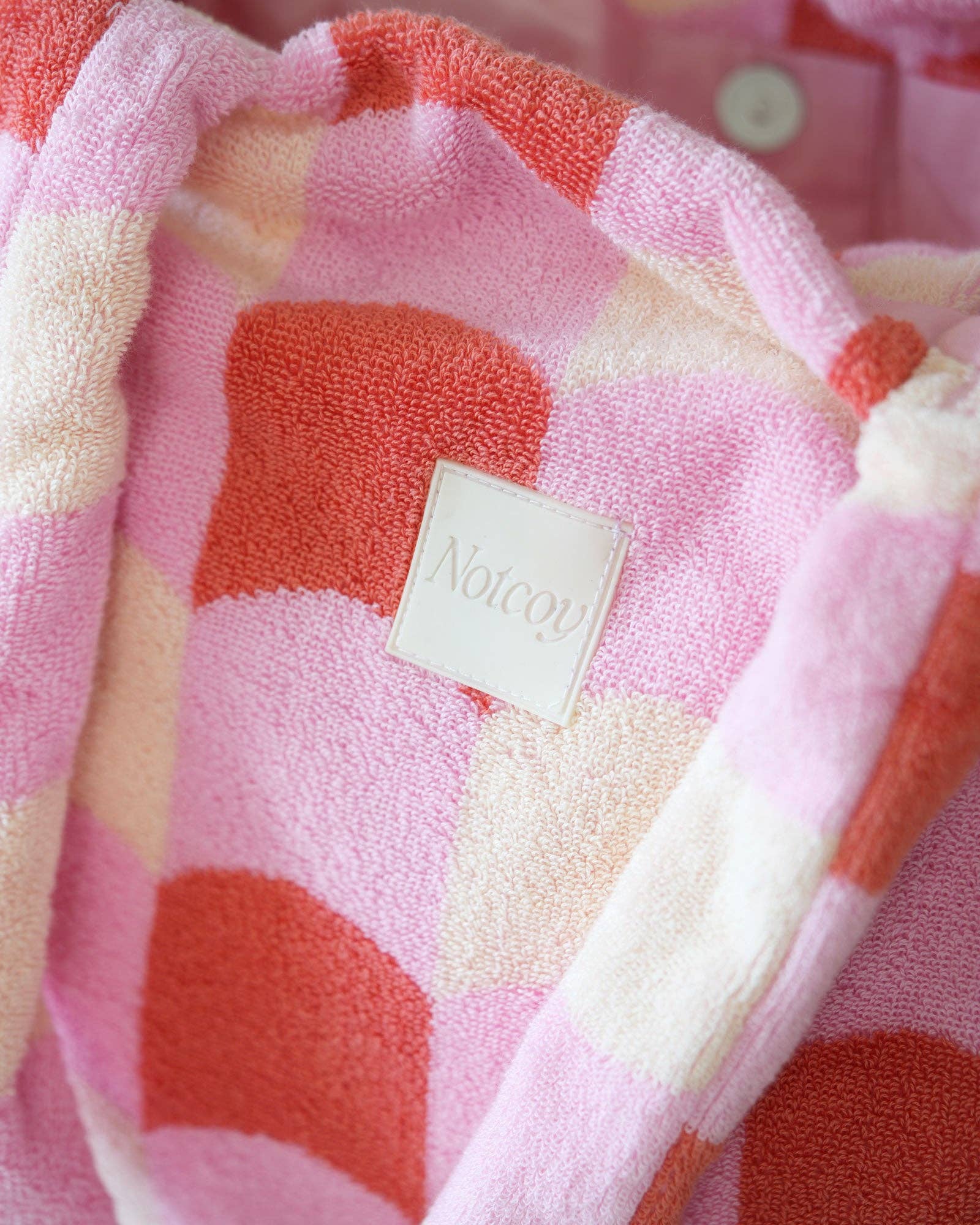 Pink and red checkered blanket with a brand label on a pink background
