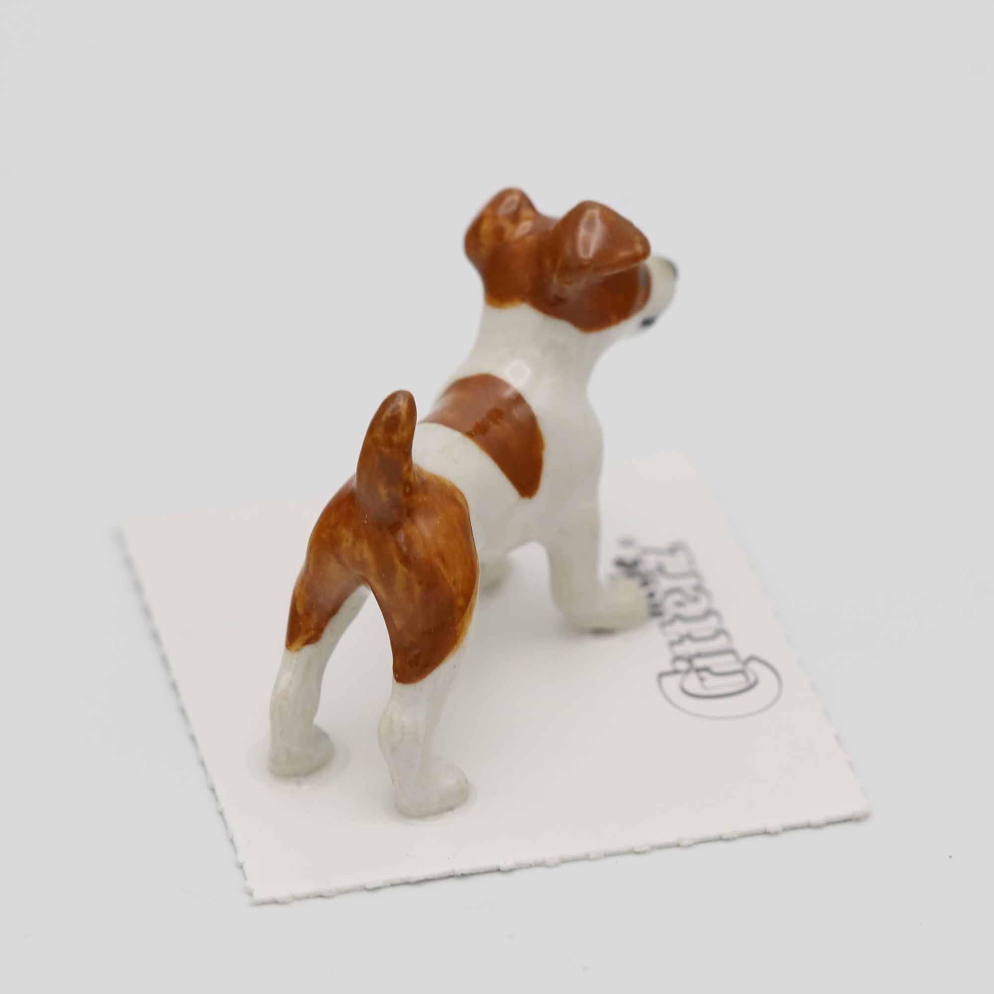 Small figurine of a brown and white dog on a white card with a brand name, on a light gray background.