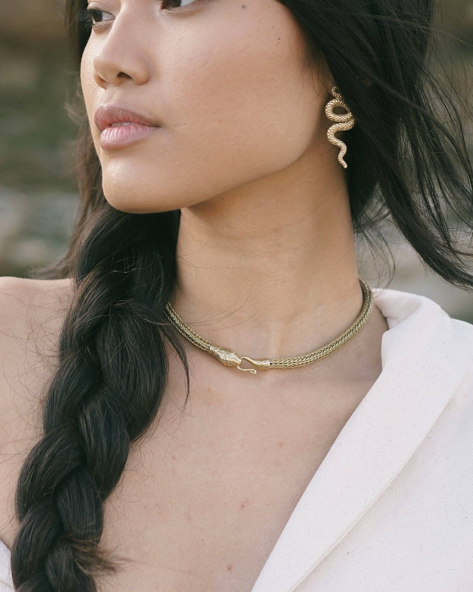 Woman with braided hair wearing a white off-shoulder top and gold jewelry against a natural background.