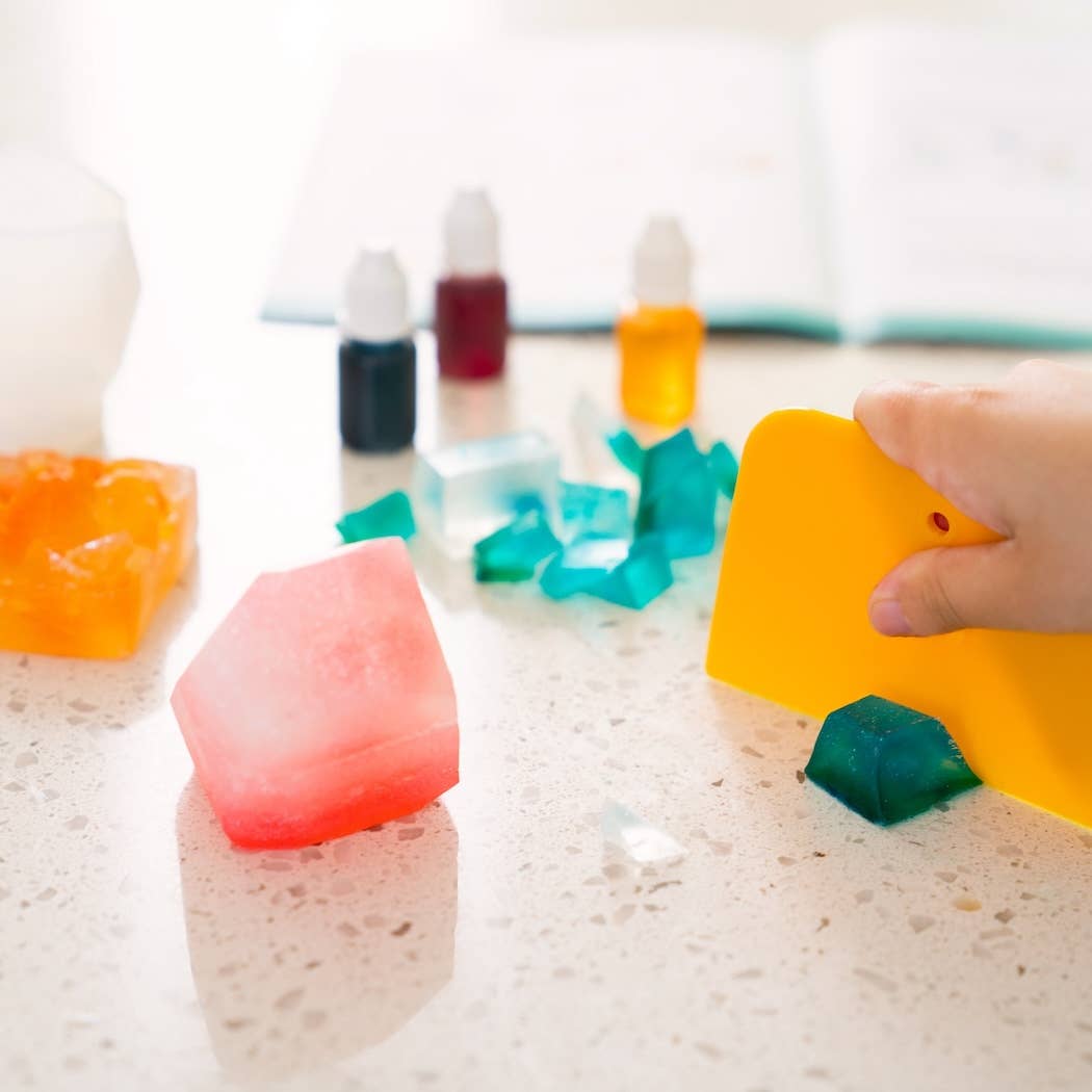 Colorful bath bombs on a white surface with a hand interacting with one of them.