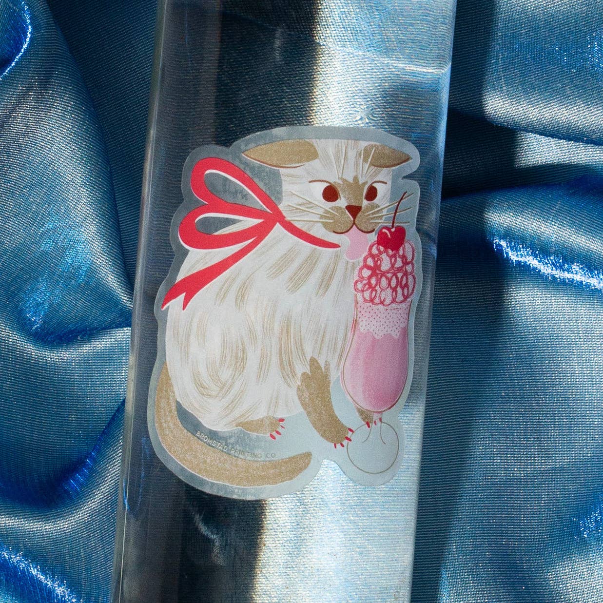 Clear plastic bottle with a cat and a sundae design on a blue satin background