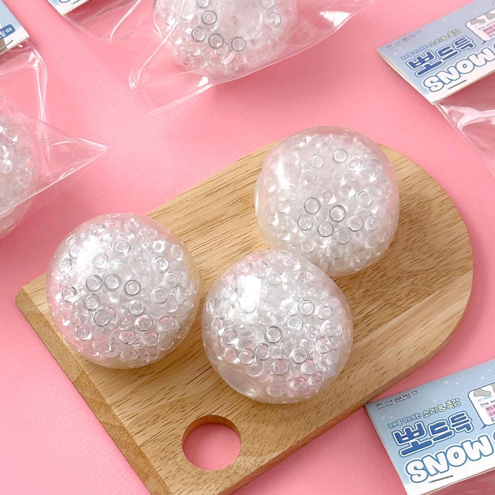 Three round, bubble-like objects on a wooden board with pink background and 'SNOW' packaging.