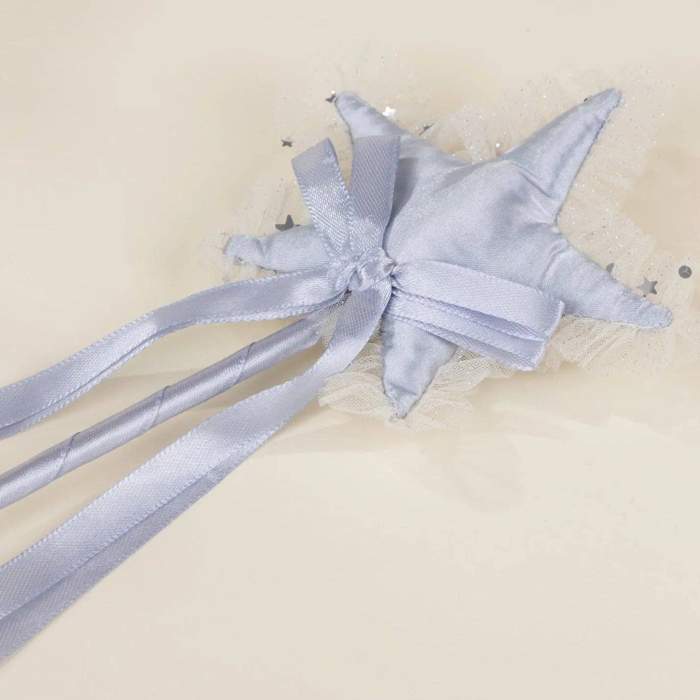 A light blue satin star-shaped hair accessory with a bow, tulle trim, and long ribbon tails, photographed on a plain cream background.