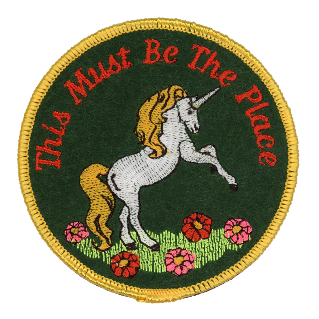 Embroidered patch with a unicorn and text 'This Must Be The Place' on a green background