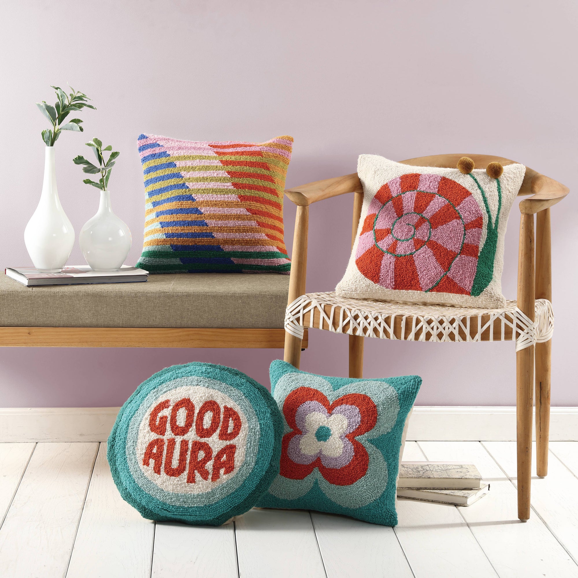 Colorful pillows with patterns and text on a chair and bench against a light purple wall.