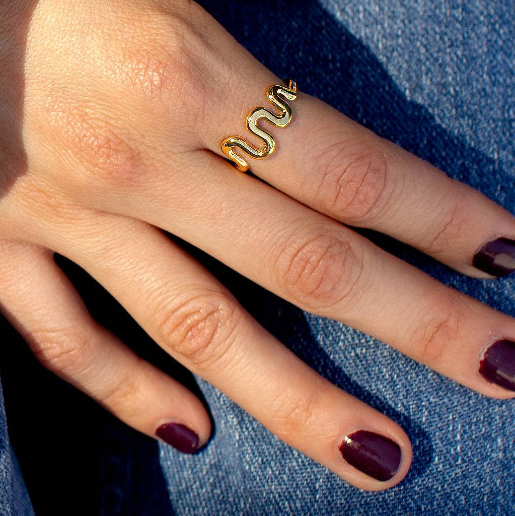 Gold snake-shaped ring on a finger with a blue denim background