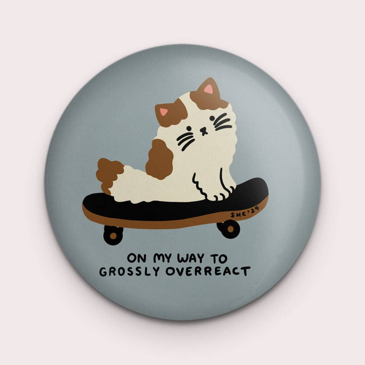 Button badge with a cat on a skateboard design and text on a light blue background