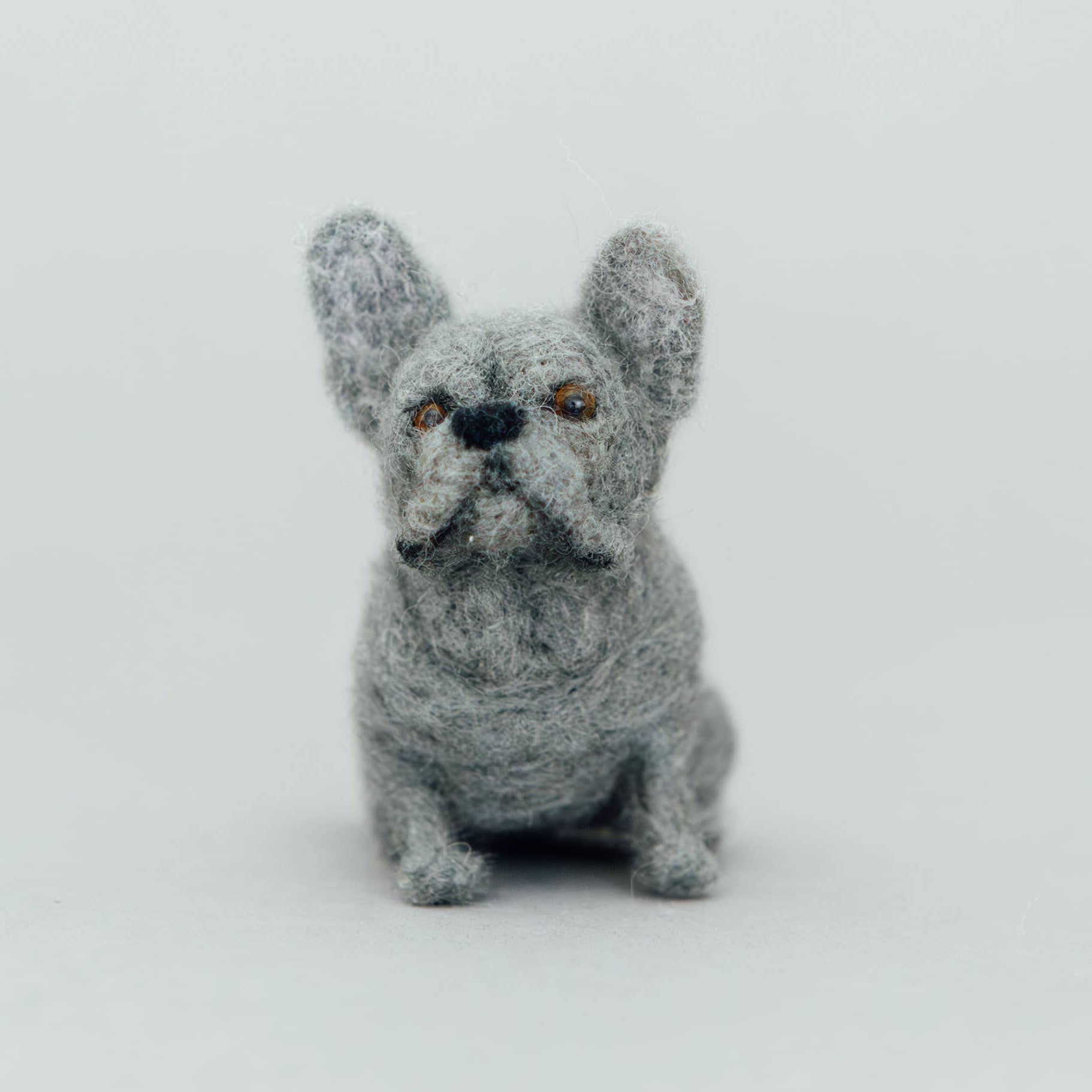 A small gray textured dog figurine, resembling a French Bulldog, centered against a seamless light gray background.