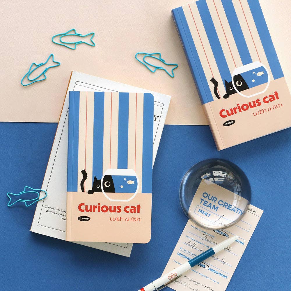 Notebooks with 'Curious cat with a fish' design on a blue surface with office supplies.