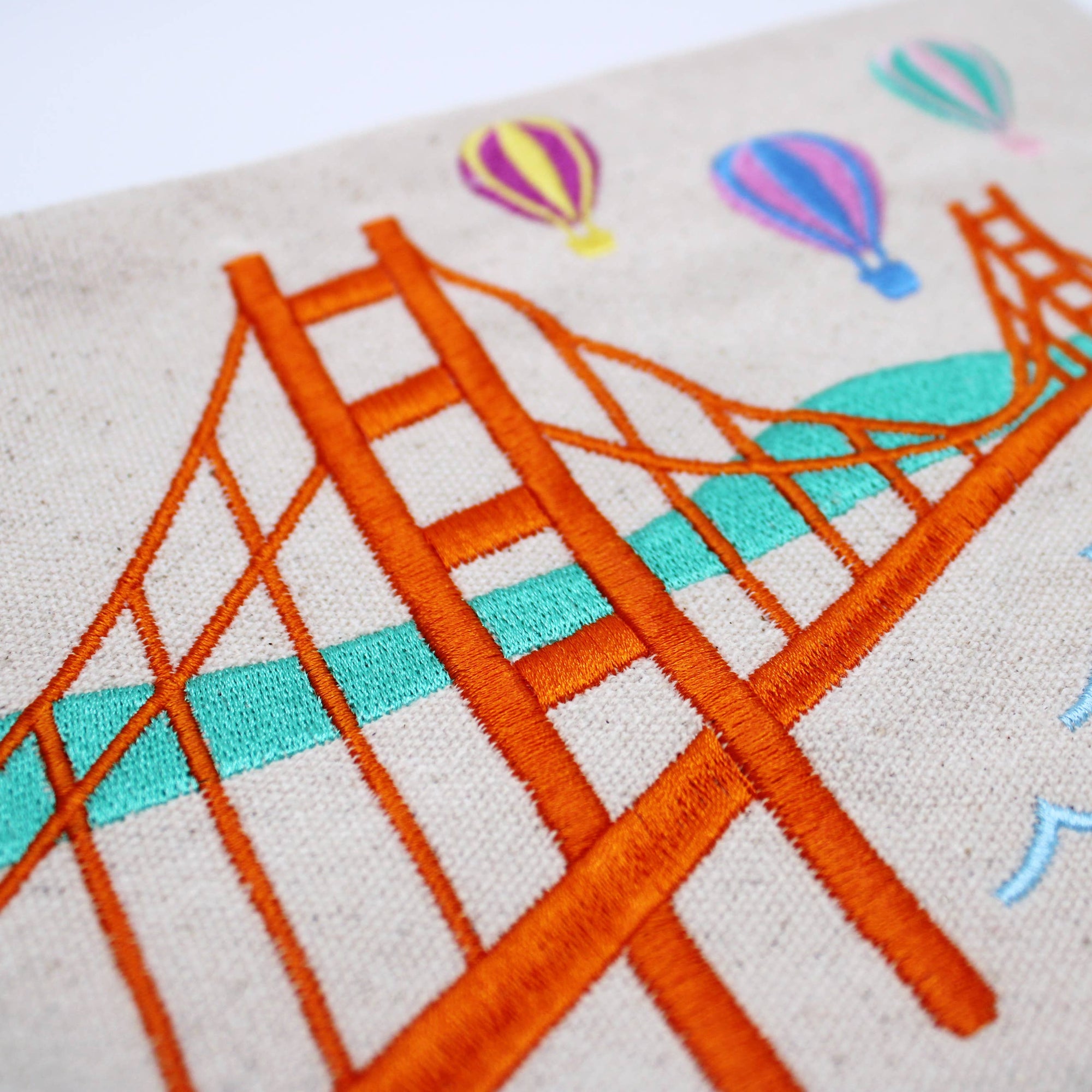 Embroidered design of a bridge and hot air balloons on fabric.