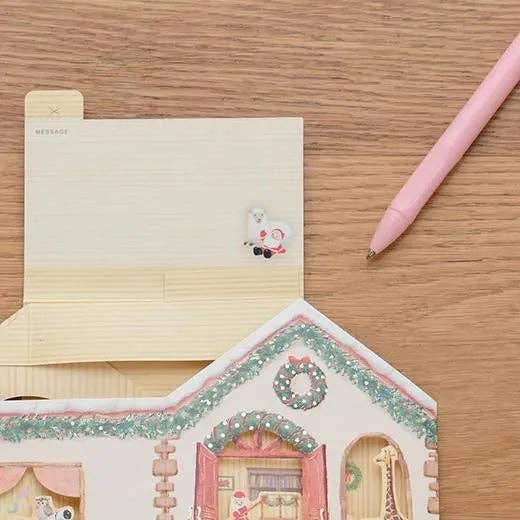 Decorative stationery set with a house-shaped notepad, pen, and small card on a wooden surface.
