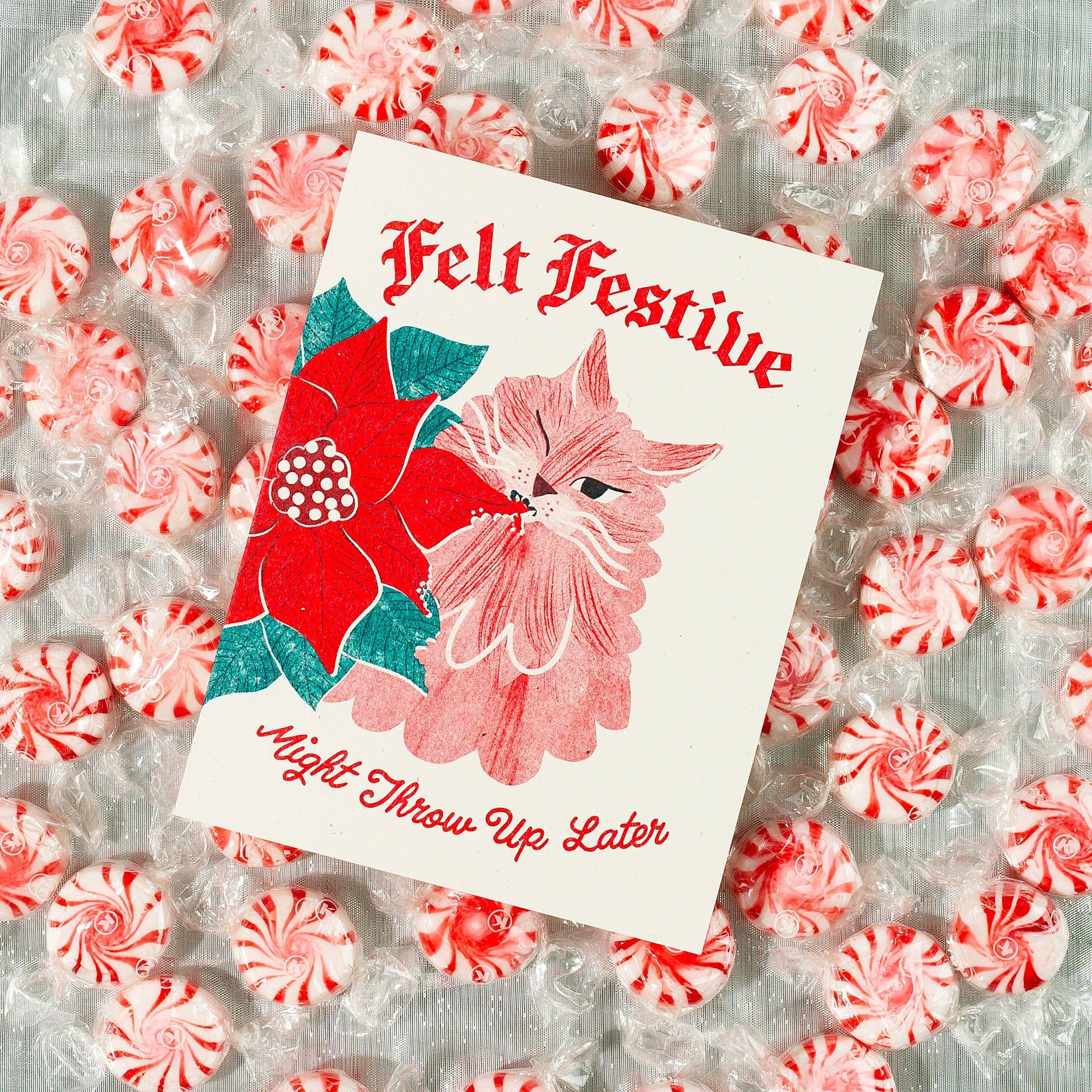 Card with a poinsettia and cat design surrounded by peppermints on a textured background