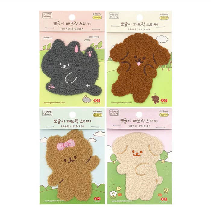 Four packaged plush fabric stickers by Glamee, featuring cartoon animal characters: a black cat, a brown puppy, a brown bear with a pink bow, and a cream puppy. Each sticker is shown on its printed backing card against a white background.