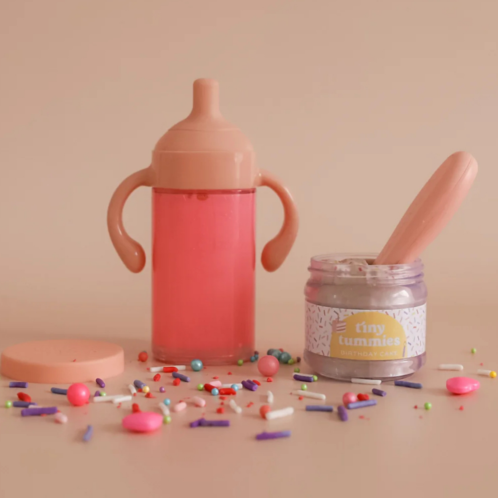 Pink sippy cup with spoon and container on a beige background