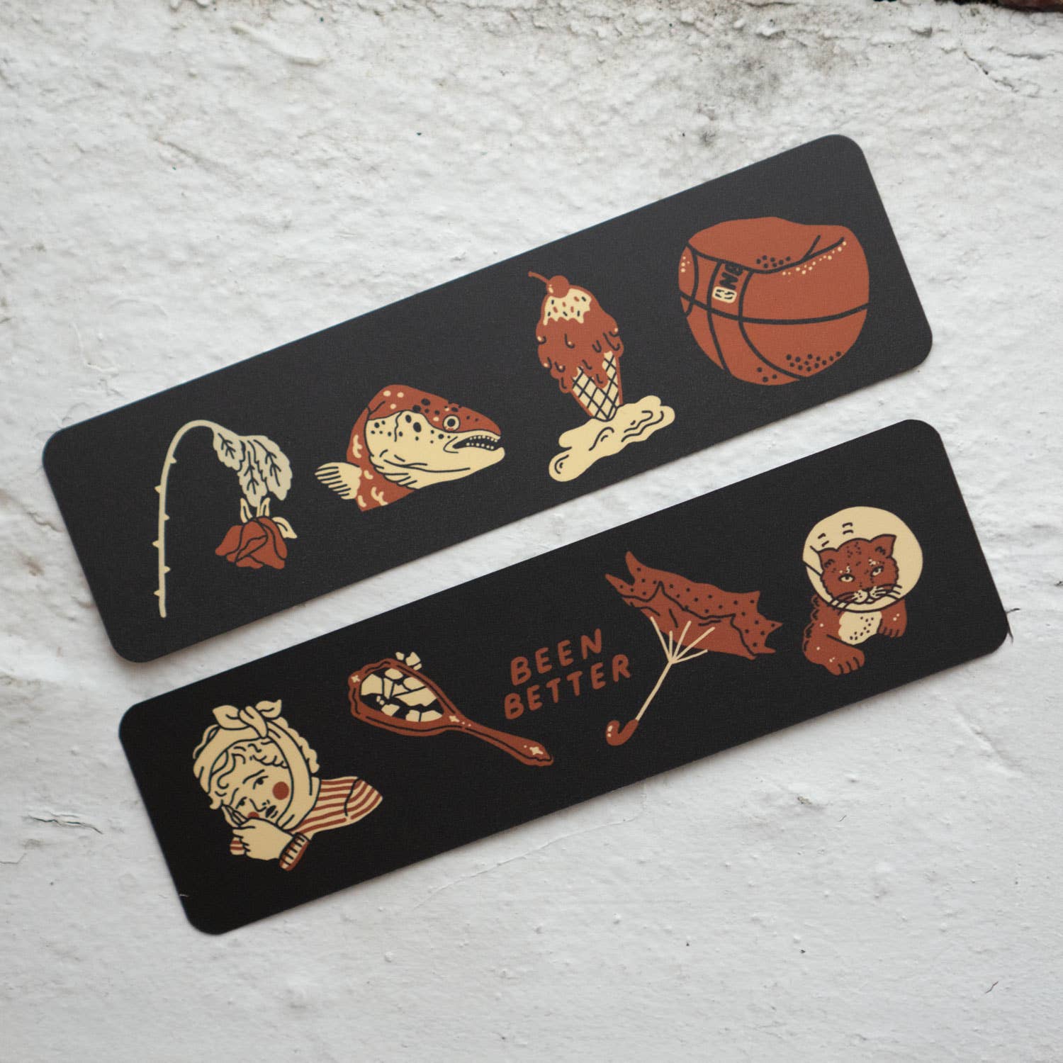 Two black bookmarks with illustrated designs on a light gray surface