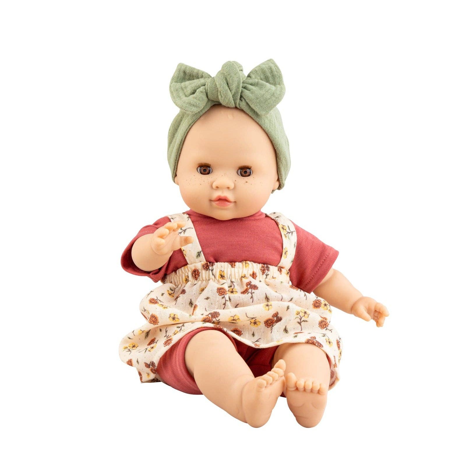 Baby doll wearing a red outfit with floral overalls and a green headband on a white background