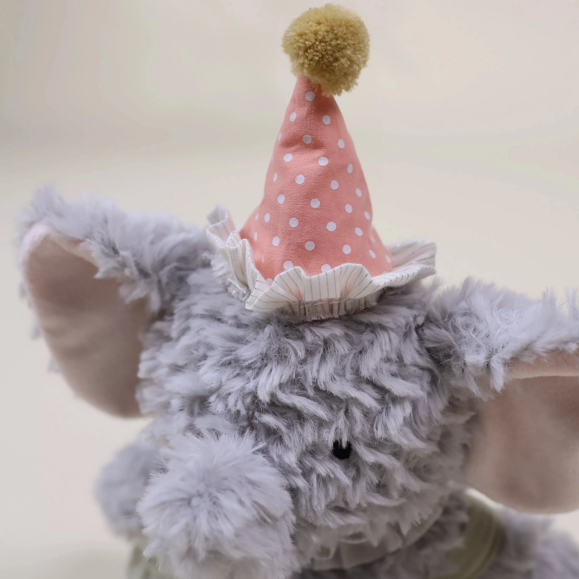 Plush elephant toy wearing a party hat with a polka dot design on a plain background