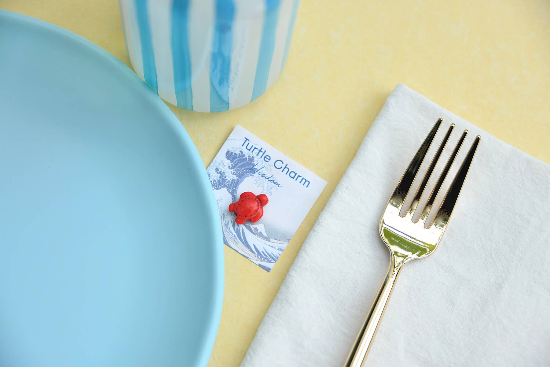 Gold fork on a white napkin with a card labeled 'Turtle Charm' on a yellow surface.