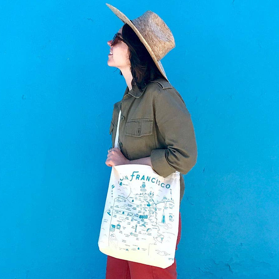 Person holding a tote bag with San Francisco design against a blue wall