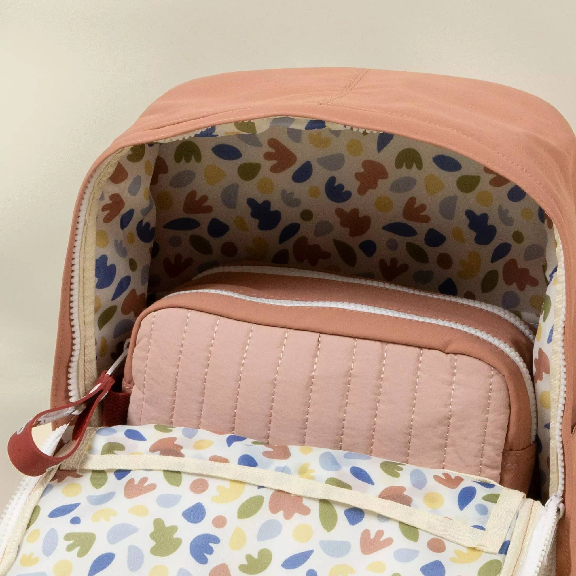 Close-up of a backpack with colorful patterned interior and quilted pink surface.
