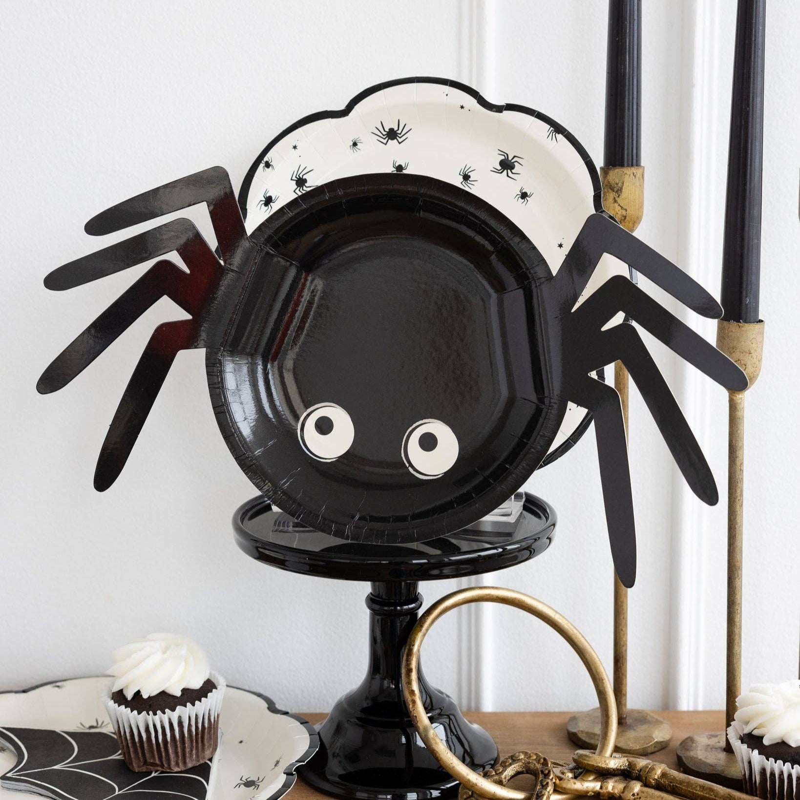 Spider-shaped plate holder with black and white design on a table with Halloween-themed decor.