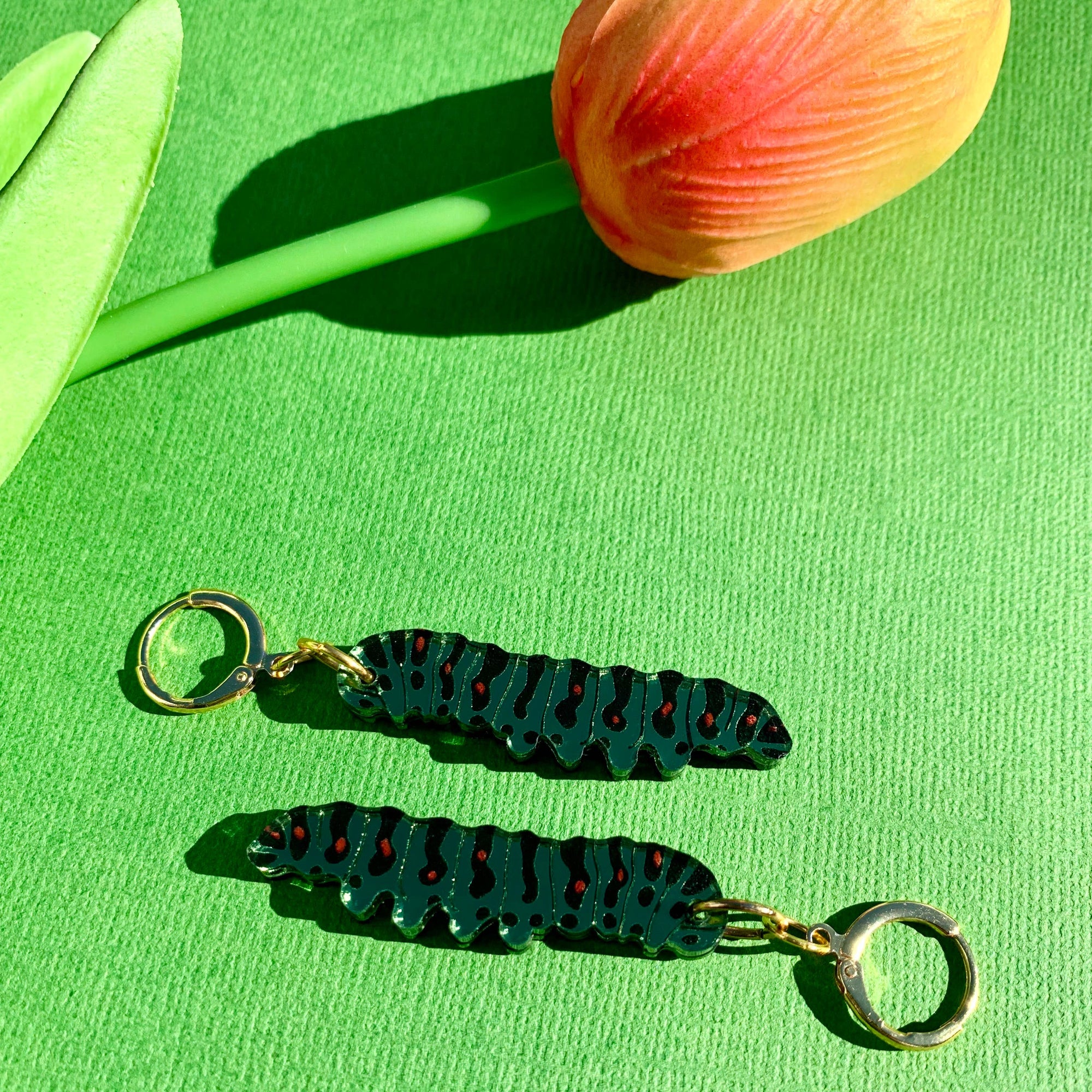 Pair of green earrings with red accents on a green background