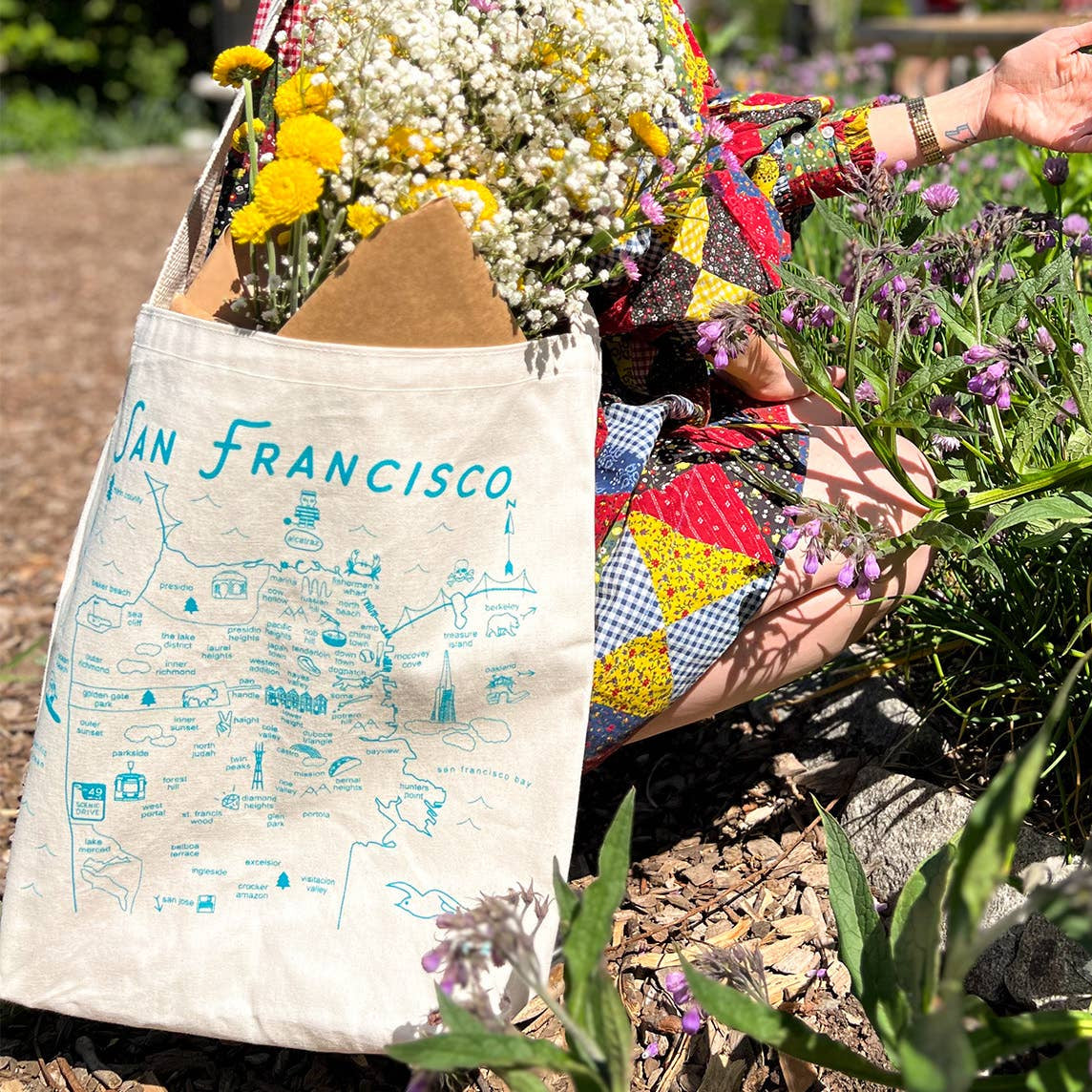 Person holding a colorful bag with a 'San Francisco' tote bag next to flowers