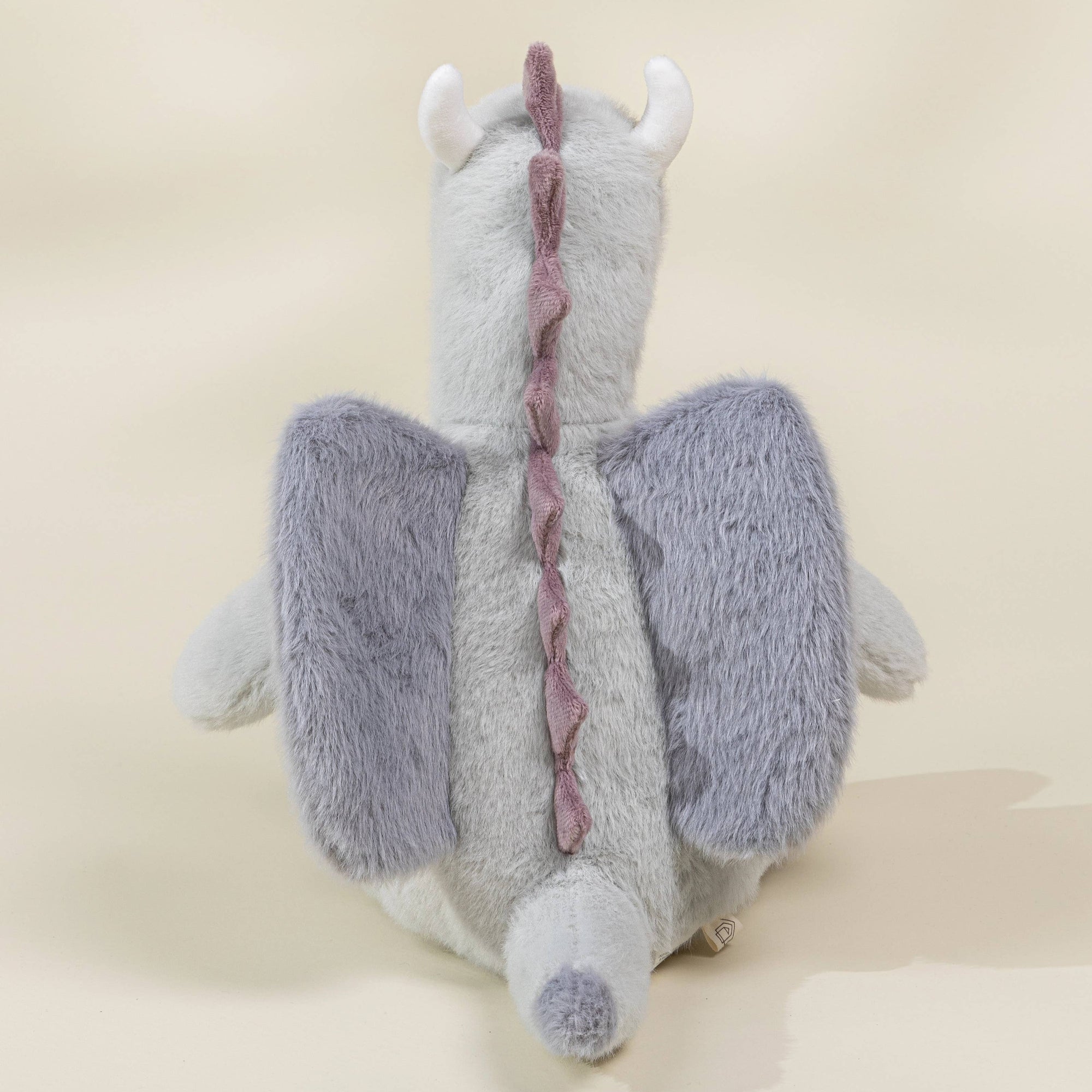 Plush toy dragon with purple wings on a beige background
