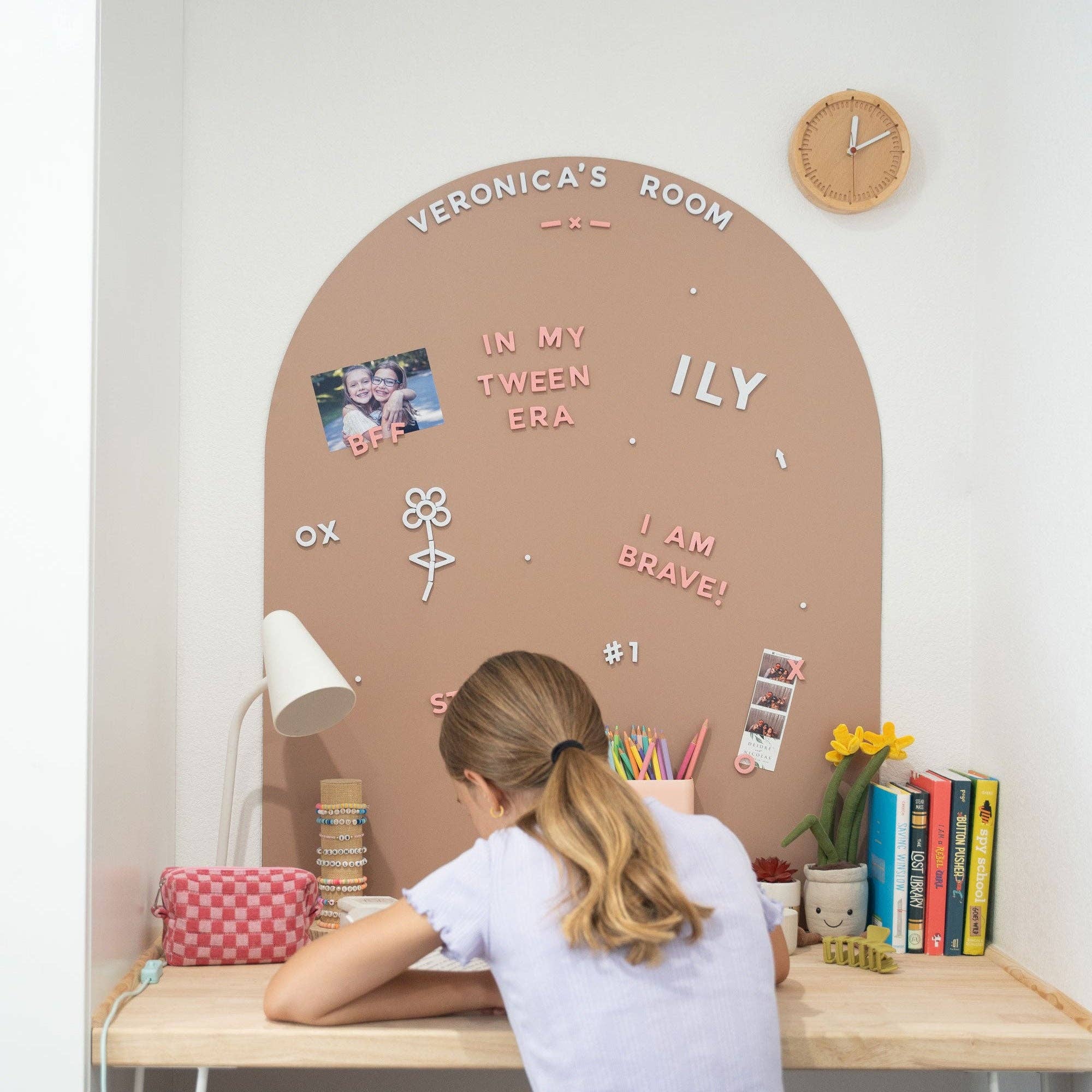 Person sitting at a desk with a personalized wall display in a room.