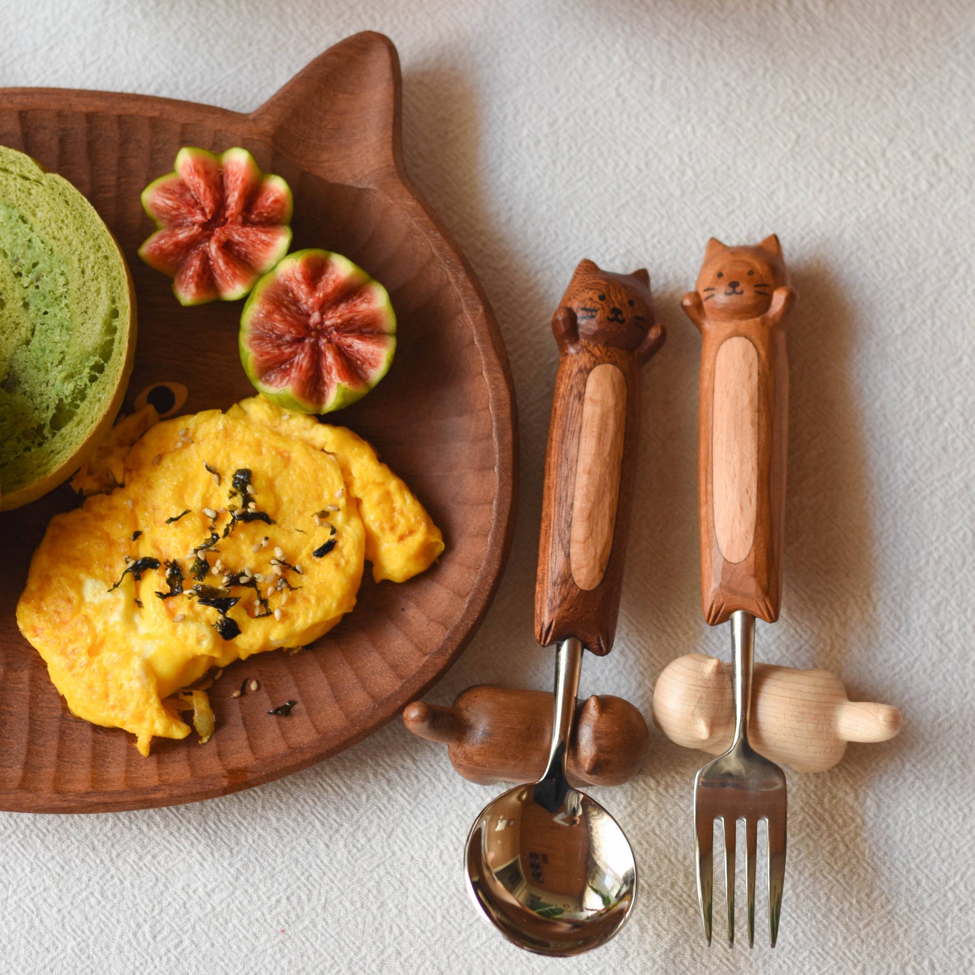 Wooden cutlery with cat handles next to a plate of food.