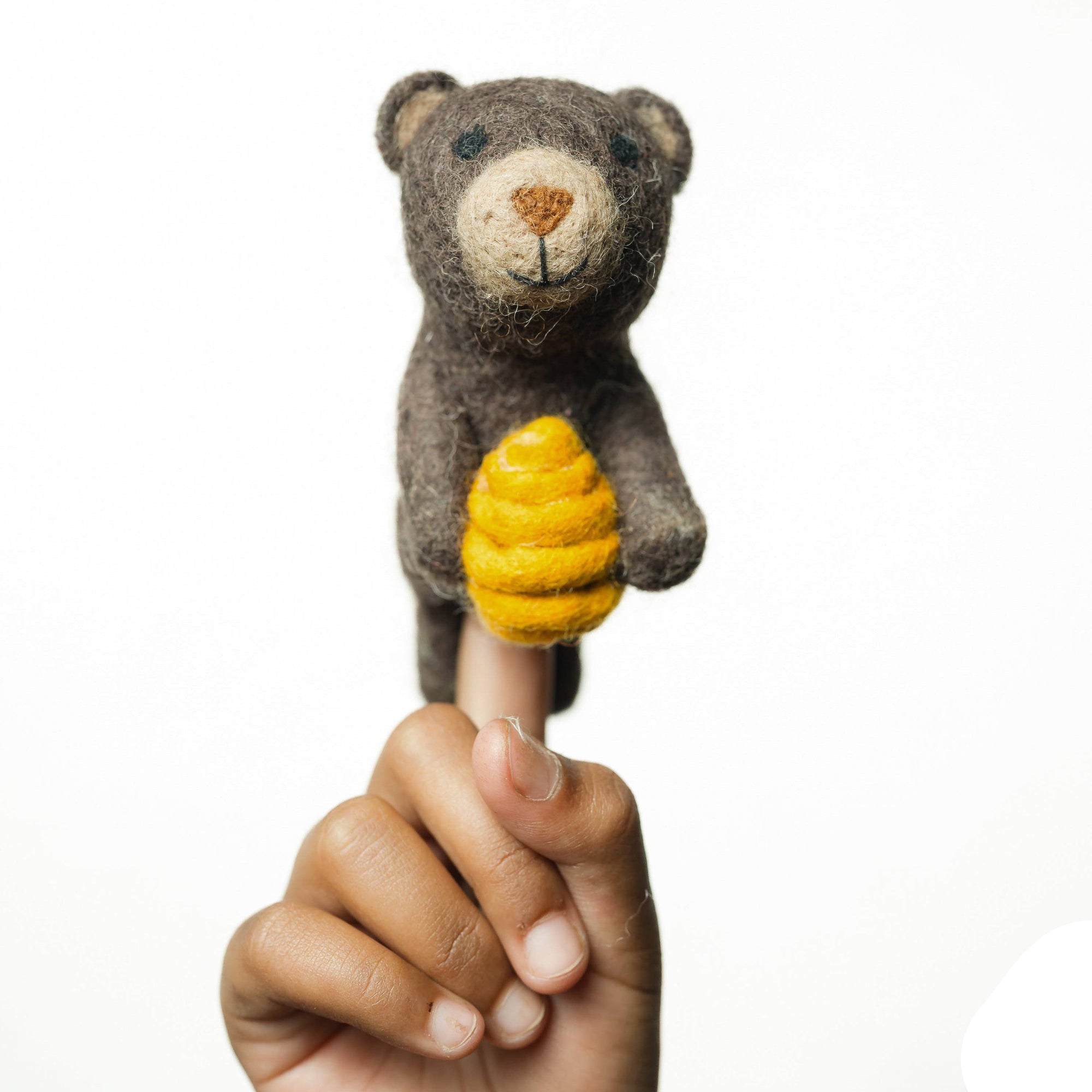 Hand holding a finger puppet of a bear with a yellow honey comb on a white background