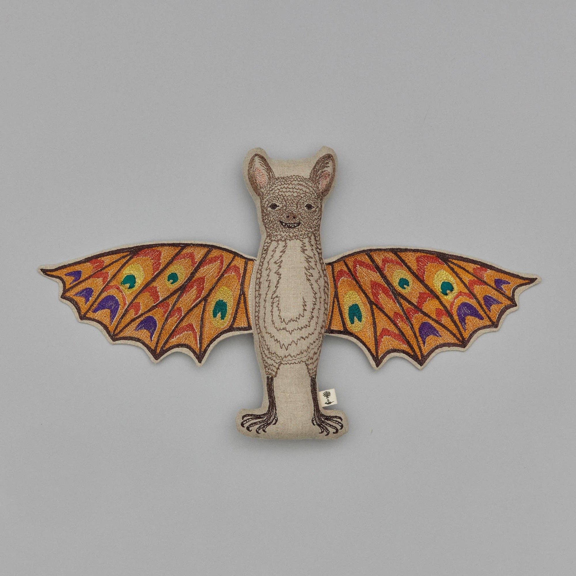 Bat-shaped plush toy with colorful wings on a gray background