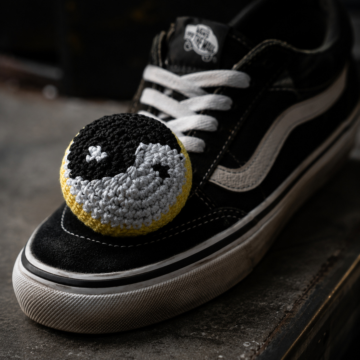 Black and white sneaker with a textured black, white, and yellow ball on a dark surface