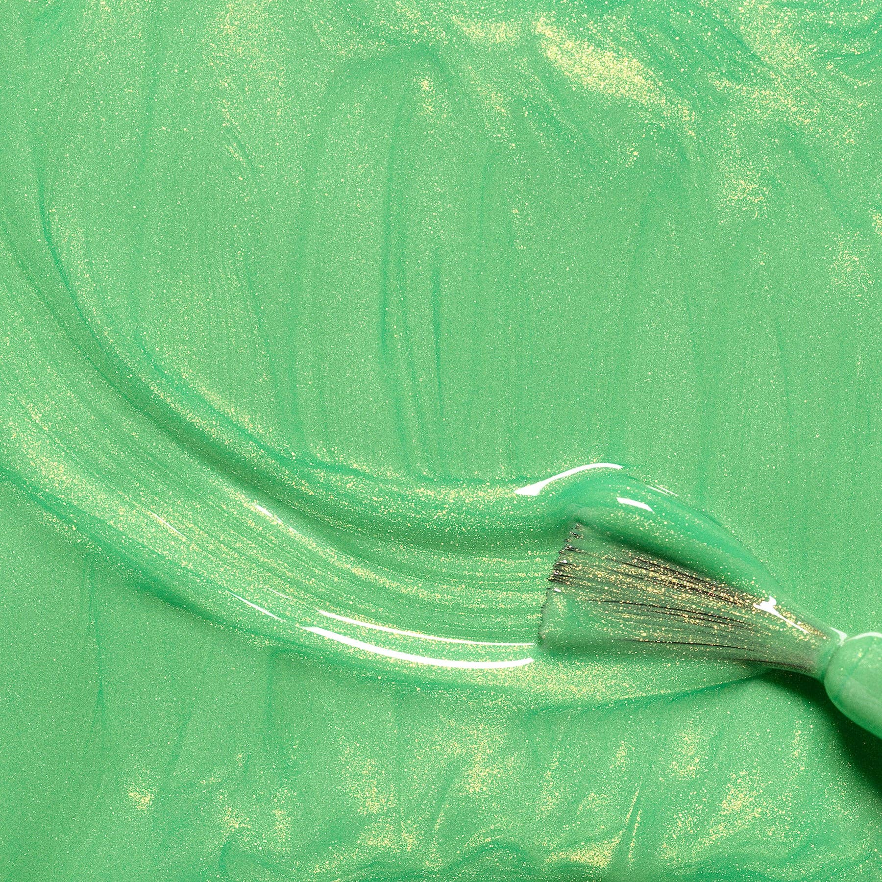 A close-up of a mint green, shimmery cosmetic cream or liquid swatch with a brush stroke on a textured background.