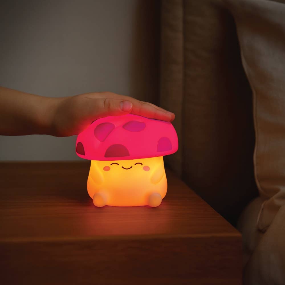 Mushroom-shaped night light with a hand touching it on a wooden surface.